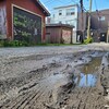 Une ruelle embouée, en arrière-plan, des garages et des poteaux électriques