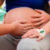 Des mains sont posées sur le ventre d'une femme enceinte.   
