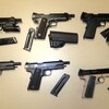 Six armes à feu illégales sont étendues sur une table.