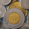 Plusieurs pièces de monnaie canadienne sur une table. Une pièce de deux dollars est posée par-dessus une pièce de un dollar et entourée de pièces de cinq cents.