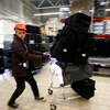 Un jeune homme d'environ 20 ans coiffé d'un casque protecteur pousse un panier d'épicerie sur lequel des paniers de livraison sont empilés.