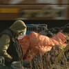 Un itinérant est assis au milieu d'un campement qui a été démoli près d'une voie ferrée.