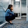 Une femme d'affaires stressée accroupie dans le couloir d'un immeuble de bureaux.