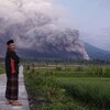 Un Indonésien en premier plan et le volcan en fumée en arrière.
