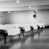 Photo d'époque en noir et blanc sur laquelle apparaissent des lits disposés dans une grande salle, avec une statue du Seigneur accrochée au mur.