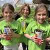Trois petites sourient à la caméra, chacune un plant en main.