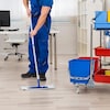 Un homme dans un uniforme de travail bleu nettoie le plancher d'un bureau avec une vadrouille.