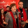 Une femme portant un manteau et un foulard rouge hausse les épaules derrière un micro lors d'une conférence de presse.