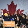 Jagmeet Singh en compagnie de sa conjointe et de militants du NPD qui agite des drapeaux du Canada sur une scène.