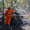 Un pompier de la SOPFEU qui arrose le sol dans une forêt.