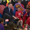 Bill Morneau enfile un soulier sous l'oeil amusé d'un groupe d'enfants.