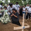 Une femme agenouillée pleure et se recueille sur la tombe d'une victime de l'attentat. Un homme la tient par les épaules, en guise de soutien.