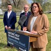 La première ministre du Manitoba, Heather Stefanson, prononce un discours devant un podium à l’extérieur au mois de juin. Derrière elle, deux hommes en complets. 