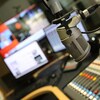 Un micro dans un studio de radio avec des écrans et une console en arrière plan. 