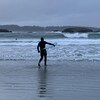 Un surfeur tient sa planche sous son bras pendant qu'il marche sur la plage en direction des vagues.