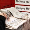 Une femme prend un exemplaire du journal Sydney Morning Herald.