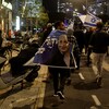 Des personnes manifestent dans une rue avec des drapeaux israéliens et des affiches.
