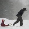 Une femme traîne un enfant assis sur une luge en pleine tempête de neige.
