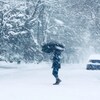 Une personne tenant un parapluie ouvert traverse une rue pendant une tempête de neige.
