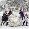 Des enfants poussent une énorme balle de neige.
