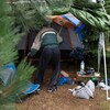 Un sans-abri à côté d'une tente installée au milieu des arbres.