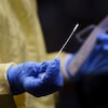 Une main recouverte d'un gant médical bleu tient un goupillon pour prélever un échantillon dans la narine d'une personne.