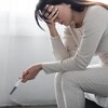 Sous le choc, une femme en pyjama est assise sur le bord de son lit, le front appuyé sur une main. Elle tient un test de grossesse autoadministré.