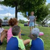 Quatre enfants dans un parc écoutent attentivement une pièce de théâtre jouée en solo. 