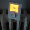 Un thermostat réglé à 19 degrés Celsius posé sur un radiateur en fer, peint en blanc, dans un appartement.