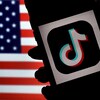 Un écran de téléphone intelligent affiche le logo de TikTok, avec le drapeau des États-Unis en arrière-plan. 