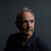 Une photo de Tim Berners-Lee, un homme aux cheveux gris avec une légère calvitie portant un veston bleu marine. Il regarde vers la droite d'un air pensif.