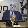 Tim Houston assis en conférence de presse devant un écran fixé au mur sur lequel apparaît le docteur Strang.