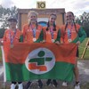 Quatre jeunes tiennent un drapeau et portent une médaille au cou en souriant.