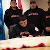 Duane Smith signe un document. Quatre personnes sont debout derrière, le 24 novembre 2021, à Inuvik, aux Territoires du Nord-Ouest.