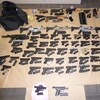 Des dizaines d'armes sont disposées sur un plancher.