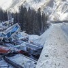 Une dizaine de wagons brisés sont empilés sur le bord d'une route enneigée.