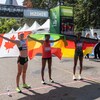 Les trois coureuses qui ont complété le marathon d'Ottawa soulèvent fièrement derrière elles le drapeau de leur pays d'origine, près de la ligne d'arrivée. 