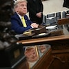 Donald Trump est installé derrière le bureau ovale, sur lequel sont notamment déposés un buste et un téléphone.