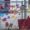 Un homme et un petit garçon sont debout, de dos, devant une clôture sur laquelle sont attachés des coeurs en papier et des messages.