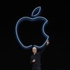 L'homme, sur scène, fait un signe de paix avec les doigts devant un logo d'Apple sur fond noir.