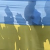 L'ombre de gens est vue derrière un drapeau ukrainien. 
