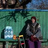 Une dame assise sur un banc près d'une clôture en bois. À côté d'elle, une béquille, une canne et des bouteilles d'eau minérale