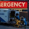 Des ambulanciers s'apprêtent à escorter un patient à l'extérieur d'une ambulance.