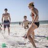 Trois jeunes adultes en maillot de bain sur la plage s'amusent à jouer au ballon avec un enfant.