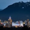 Le centre-ville de Vancouver illuminé à l'approche de la nuit avec d'immenses montagnes au loin.