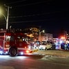 Un véhicule de pompiers est sur une scène d'incendie dans un stationnement d'un garage, où trois véhicules ont été incendiés. 