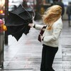Une femme aux cheveux emportés par le vent a du mal à tenir son parapluie.