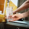 Des mains remplissent un verre d'eau à un robinet d'évier.