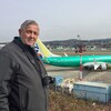 Un homme muni d'un appareil photo pose devant un tarmac sur lequel est posé un avion 737 MAX 8.