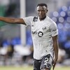 Un joueur de soccer vêtu d'un maillot gris lève un bras. 